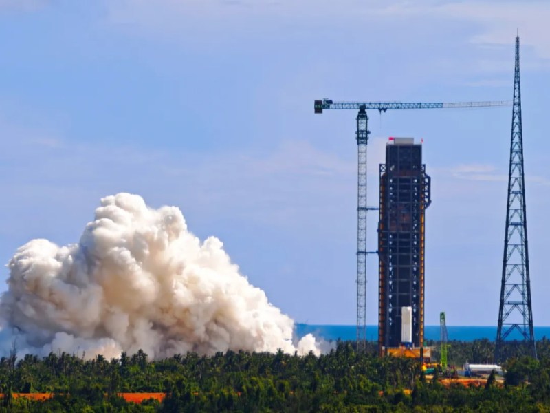 Plumes of exhaust rise above trees during a tethered hot-fire test of a Long March 10 first stage at the Wenchang Space Launch Site in Hainan, China, September 12, 2025. The test stand and service tower are visible with cranes and support structures in the background.