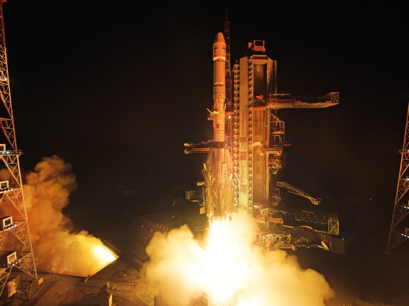 An Indian Space Research Organisation (ISRO) Geosynchronous Satellite Launch Vehicle (GSLV) lifts off from the Satish Dhawan Space Centre at night, carrying the NVS-02 navigation satellite. Bright flames and thick plumes of smoke erupt from the rocket’s engines, illuminating the launch pad against the dark sky. The towering metal launch infrastructure and support structures are visible, framing the ascending vehicle.