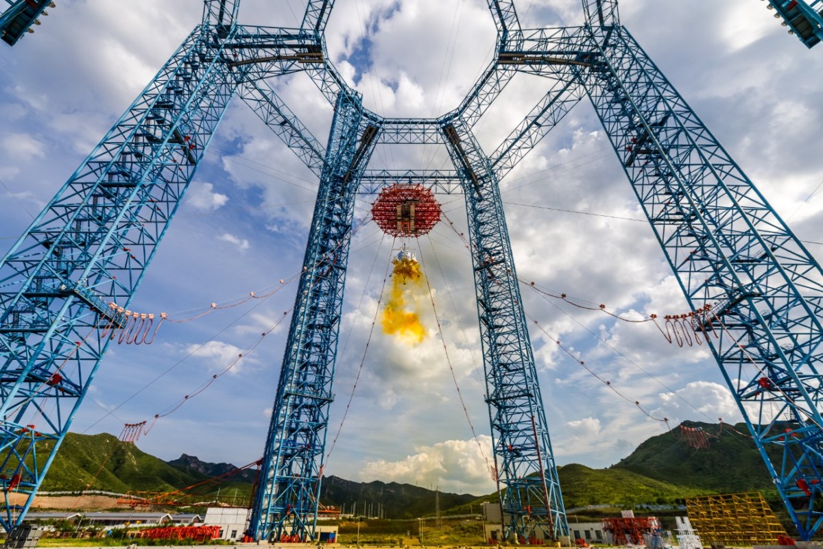 China’s Lanyue crewed lunar lander undergoing a landing and ascent test at the extraterrestrial celestial body landing test facility in Huailai, Hebei Province, on August 6, 2025. The lander is suspended from a large steel tower structure and firing its thrusters, producing a yellow exhaust plume characteristic of hypergolic propellants.