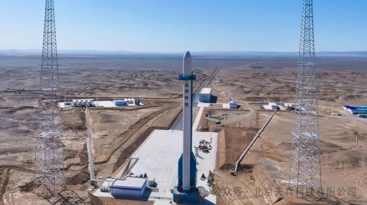 Full-scale mockup of Space Pioneer's Tianlong-3 rocket stands vertically on a newly completed launch pad at the Dongfeng Commercial Space Innovation Test Zone, located in the desert landscape of Jiuquan Satellite Launch Center. The launch pad is equipped with support towers, fueling infrastructure, and ground facilities visible under clear blue skies.