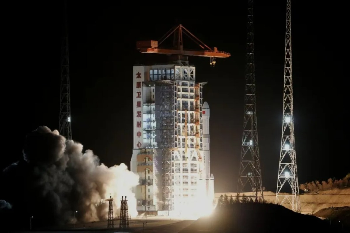 A Long March 6A rocket lifts off at night from the Taiyuan Satellite Launch Center, China, with bright exhaust and smoke plumes illuminating the launch pad tower bearing Chinese characters.